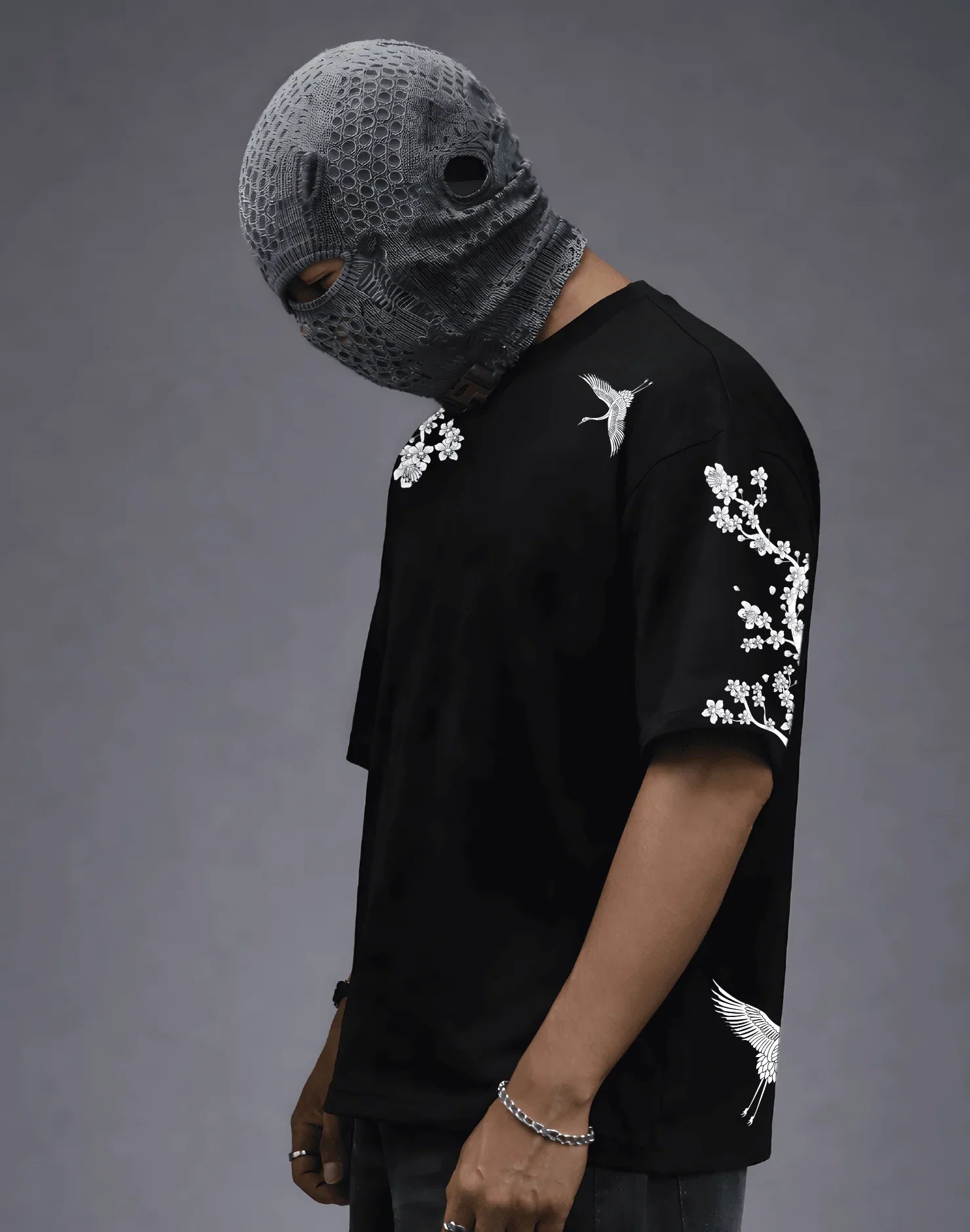 Black graphic tee with white crane and cherry blossom print, paired with textured face mask for edgy streetwear style.