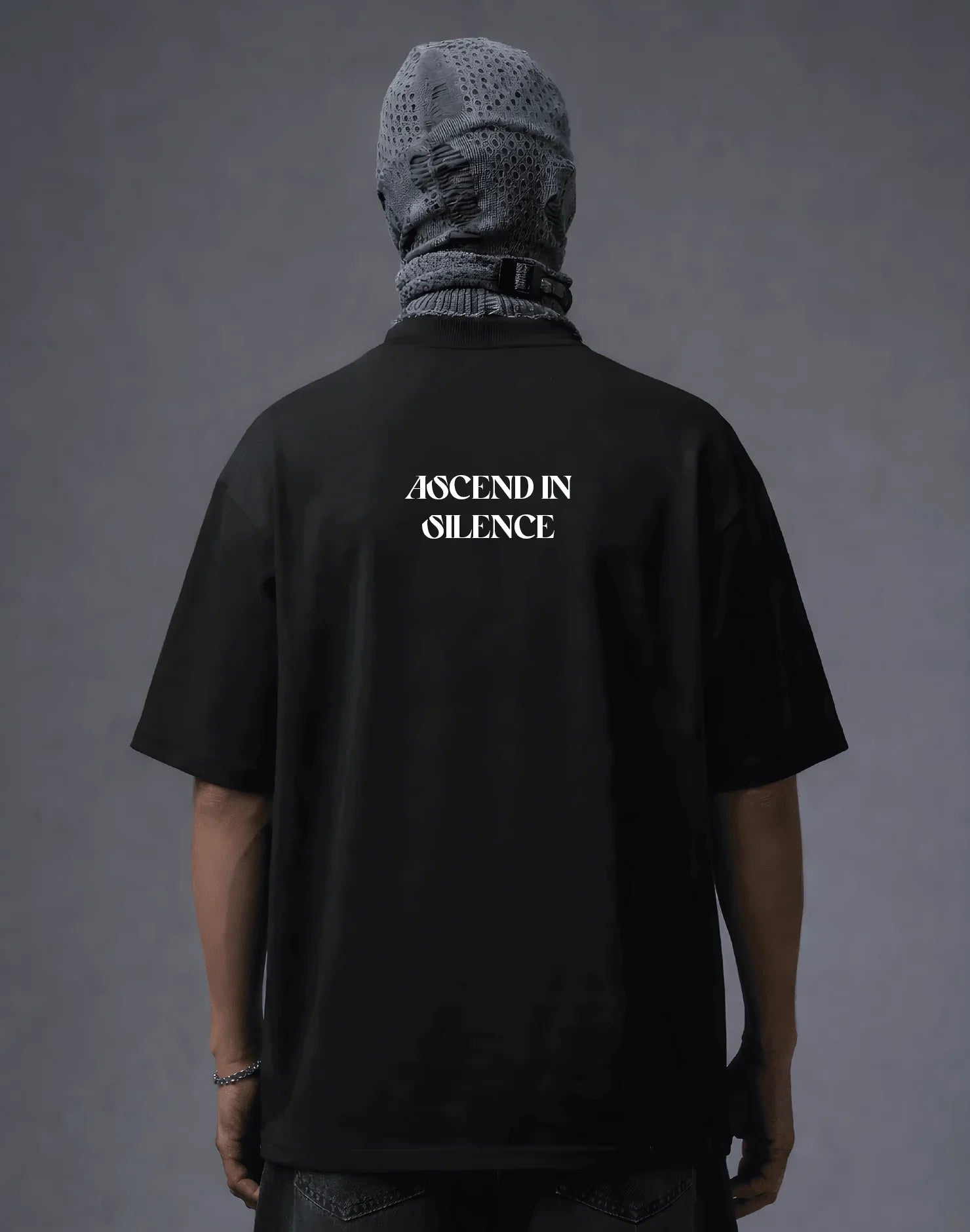 Black oversized t-shirt with 'ASCEND IN SILENCE' text, worn with mesh headwear, modern streetwear style