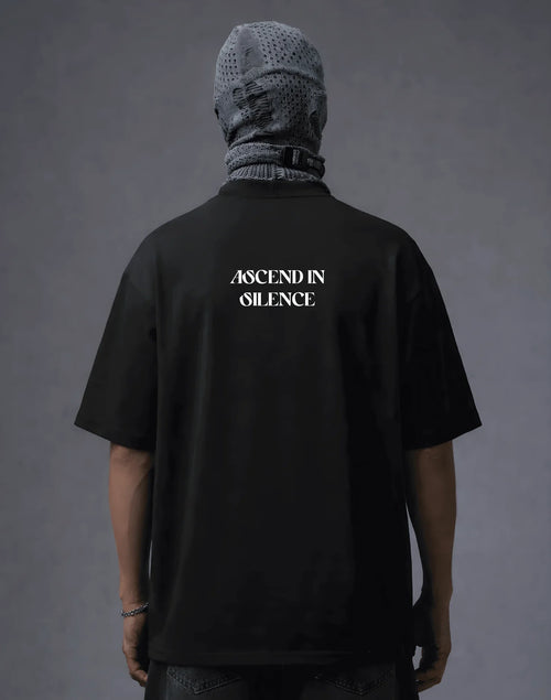 Black oversized t-shirt with 'ASCEND IN SILENCE' text, worn with mesh headwear, modern streetwear style